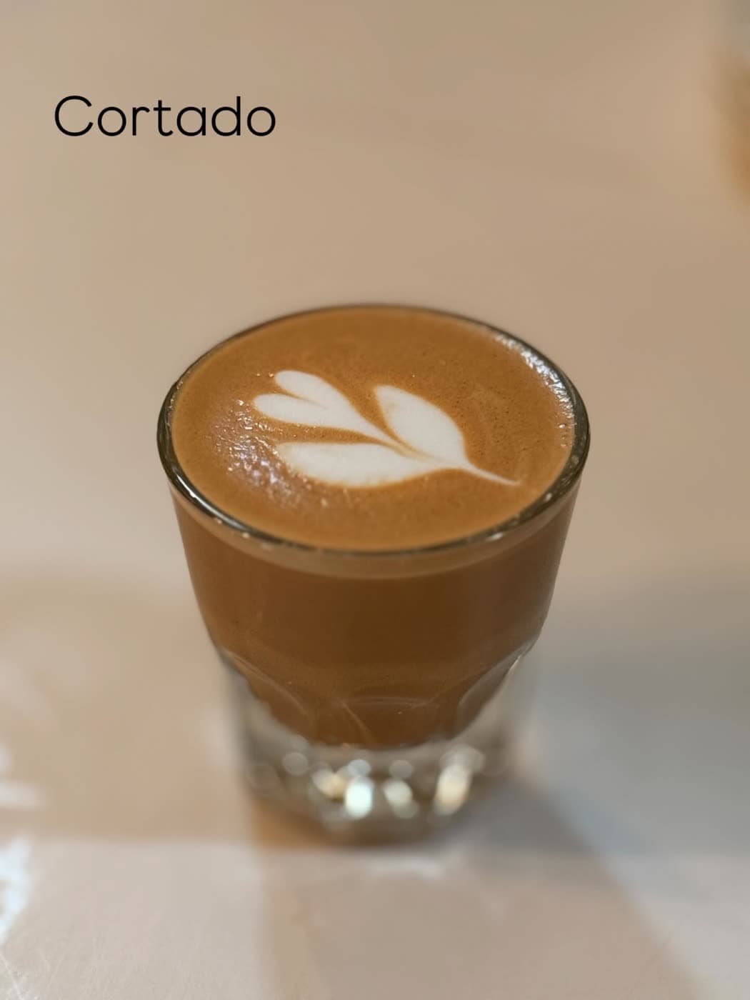 A cortado in a small glass with a leaf-pattern latte art design on top.