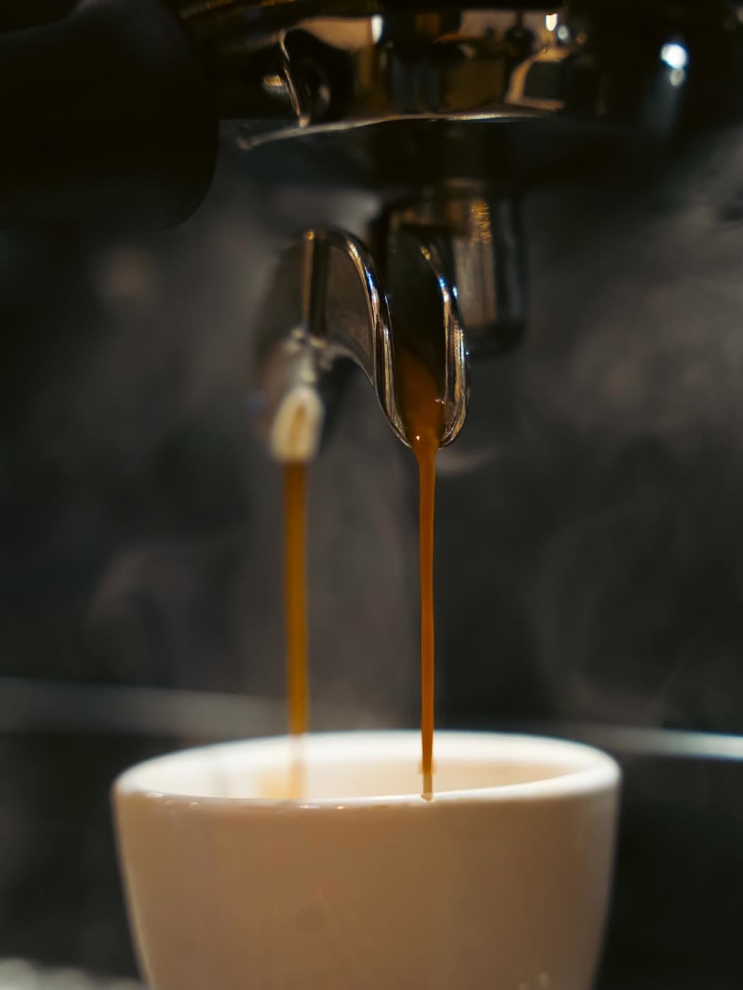 A close, moody shot of espresso pouring from a portafilter into a white cup.