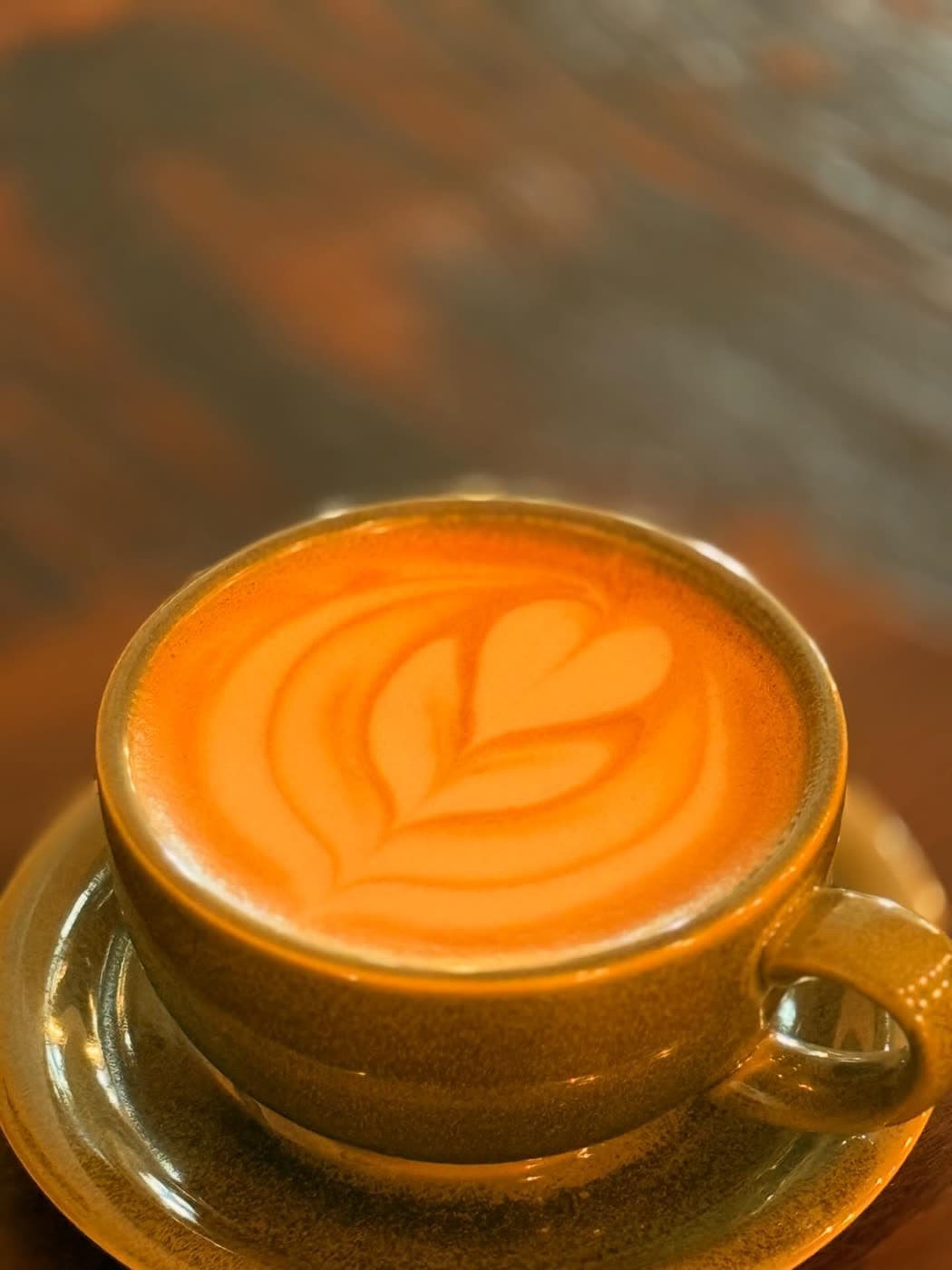A ceramic cup of coffee with heart-shaped latte art sits on a wooden table.