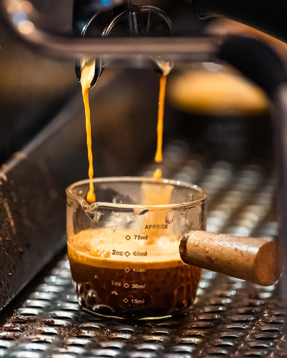 Espresso streams from a portafilter into a measuring glass on an espresso machine.
