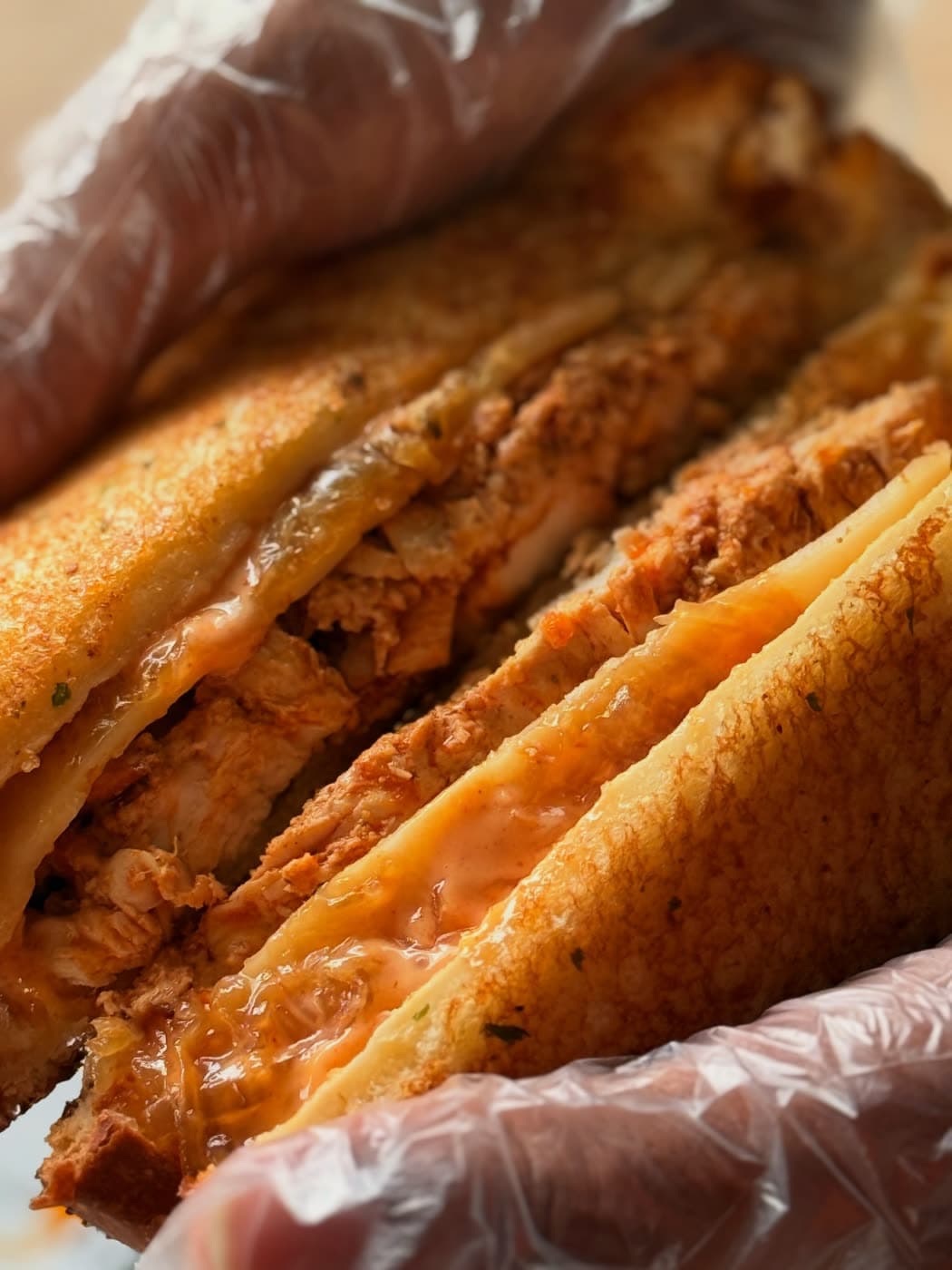 A close view of a grilled buffalo chicken toastie with glossy sauce, held in a gloved hand