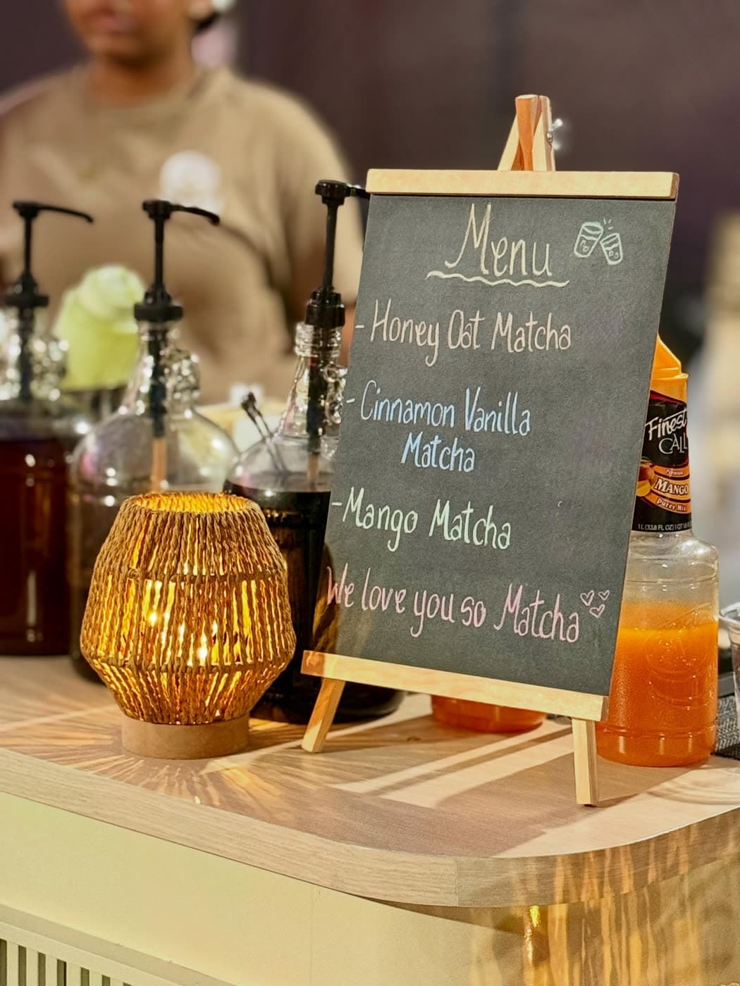 A lantern-lit cart counter with a chalkboard matcha menu, syrup pumps and glass carafes