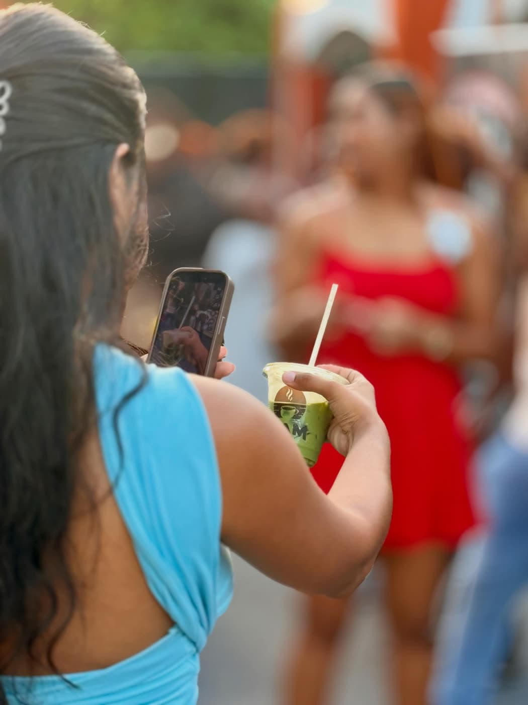 A customer films on her phone while holding a branded matcha in golden-hour light