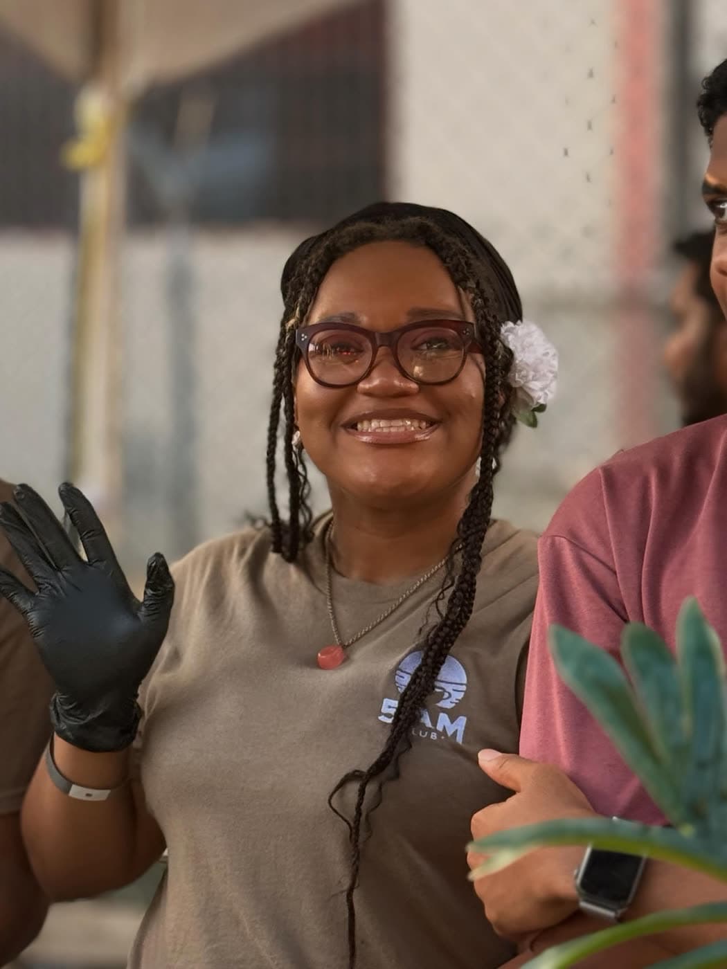 A 5AM staff member waves a gloved hand, a flower in her hair, lit by warm evening light